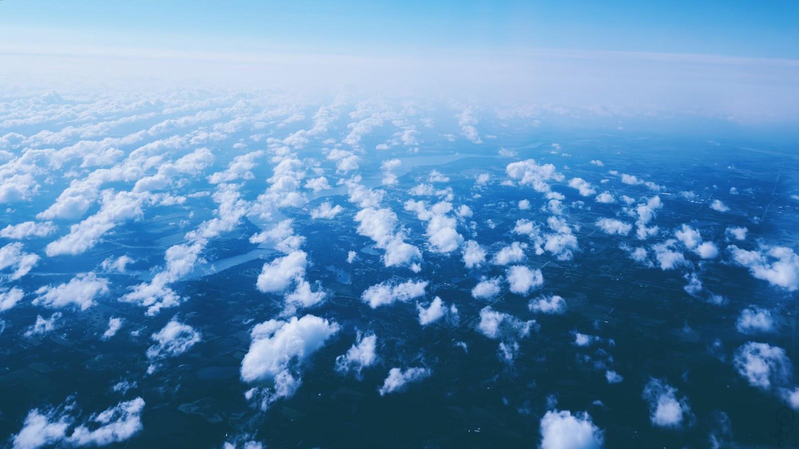 A sea of scattered clouds covers the land beneath.